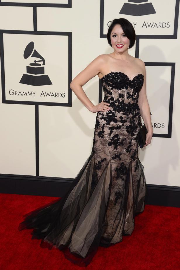 Eine Frau in einem trägerlosen Kleid mit Spitze posiert vor dem Hintergrund der Grammy Awards.