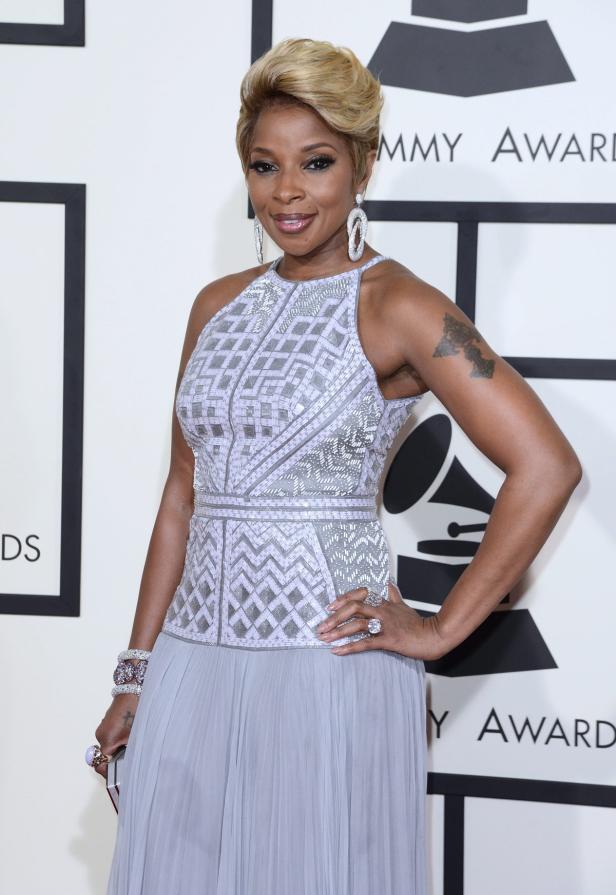 Mary J. Blige posiert auf dem roten Teppich in einem eleganten, hellgrauen Kleid.
