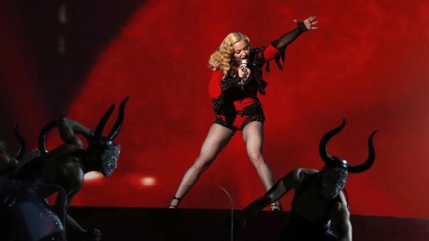 Madonna tritt in einem roten Bühnenoutfit mit Tänzern mit Hörnern auf.