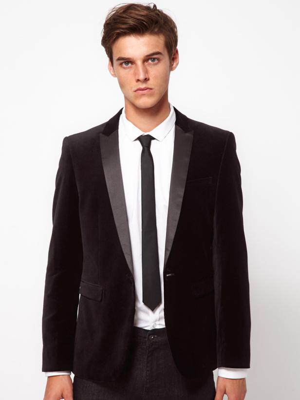 Ein Mann mit dunklem Haar trägt einen schwarzen Samtanzug mit schmaler Krawatte.