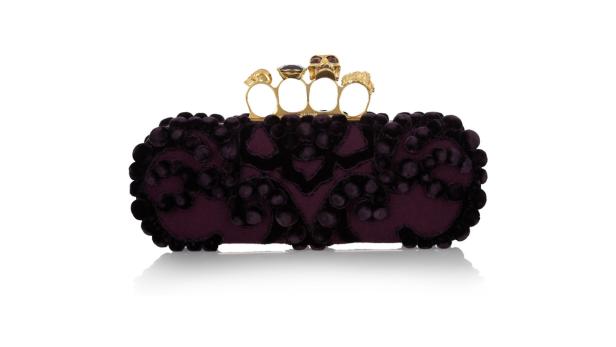 Eine verzierte, auberginefarbene Clutch mit goldenen Totenkopf-Verzierungen.