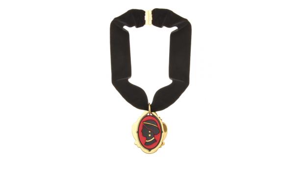 Eine Halskette mit einem schwarzen Samtband und einem goldenen Anhänger mit einem roten Profilbild.