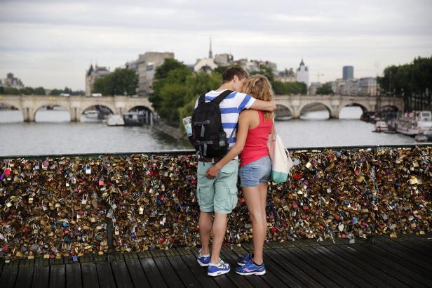 Ein Paar umarmt sich auf einer Brücke in Paris, deren Geländer mit Liebesschlössern behangen ist.
