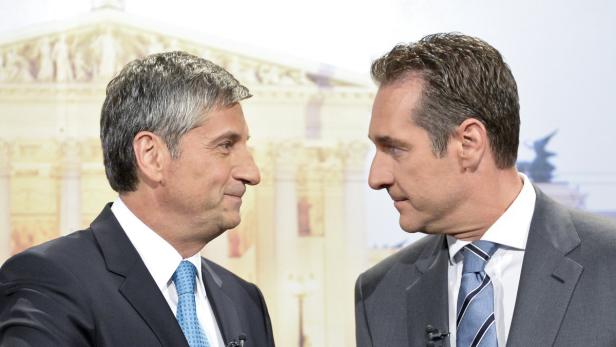 Zwei Männer in Anzügen stehen sich vor einem Gebäude gegenüber.