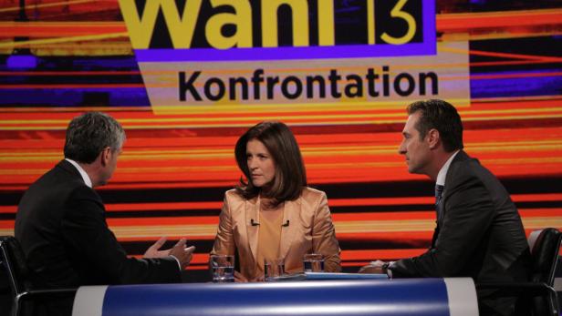 Drei Personen sitzen an einem Tisch vor dem Hintergrund einer „Wahl 13“-Konfrontation.