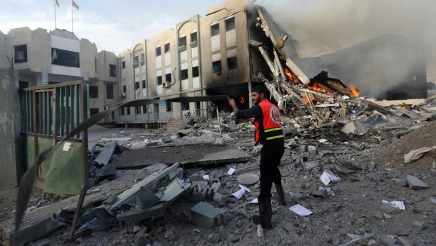 Ein Helfer steht vor einem zerstörten Gebäude, aus dem Rauch und Flammen aufsteigen.