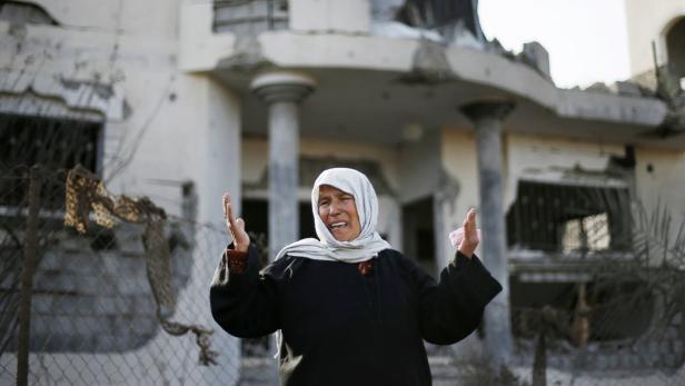 Eine weinende Frau steht vor einem zerstörten Gebäude.