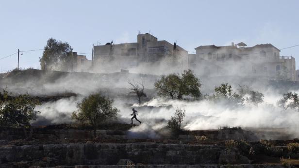 Eine Person rennt durch eine rauchverhüllte Landschaft mit Häusern im Hintergrund.
