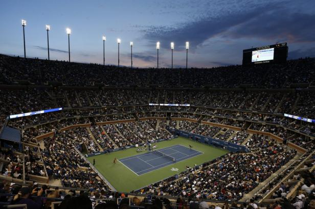 Blick auf ein Tennismatch in einem vollbesetzten Stadion bei Dämmerung.