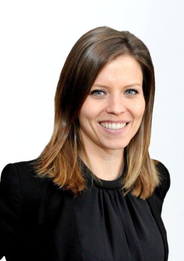 Eine Frau mit braunem Haar und blauen Augen lächelt in die Kamera.