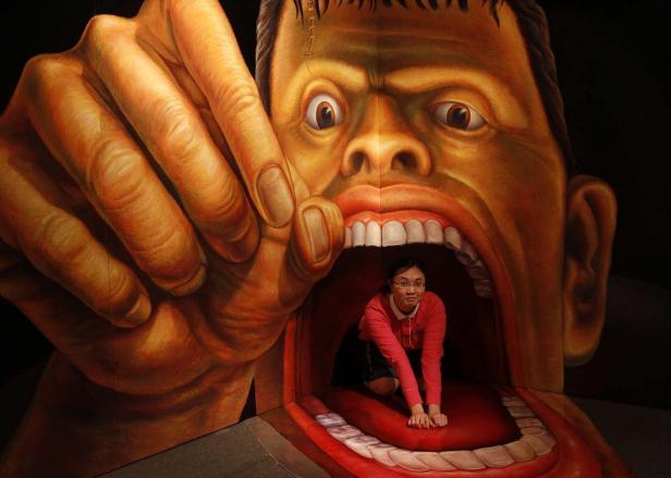 Eine Frau kniet im geöffneten Mund einer Frankenstein-Monster-Installation.