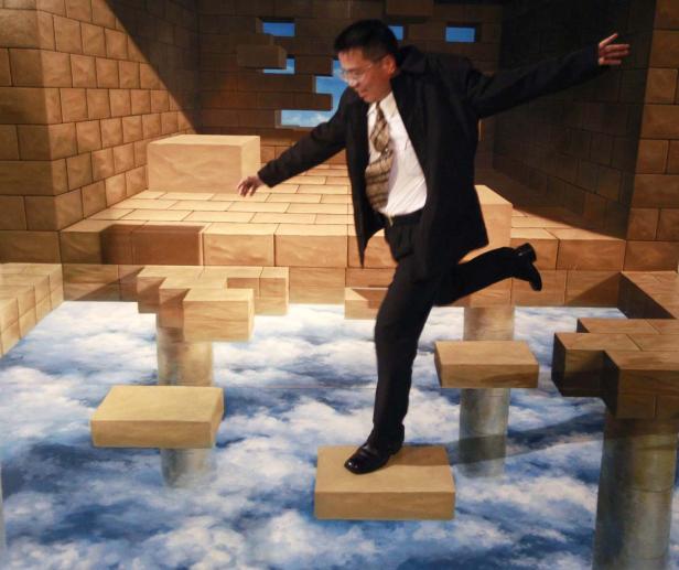 Ein Mann in Anzug balanciert auf einer optischen Täuschung, die wie schwebende Plattformen aussieht.