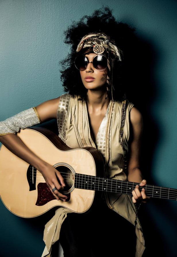 Eine Frau mit Afro-Frisur und Sonnenbrille spielt Gitarre.