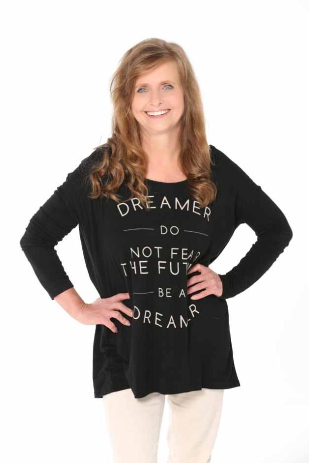Eine Frau mit lockigem Haar trägt ein schwarzes T-Shirt mit der Aufschrift „Dreamer“.
