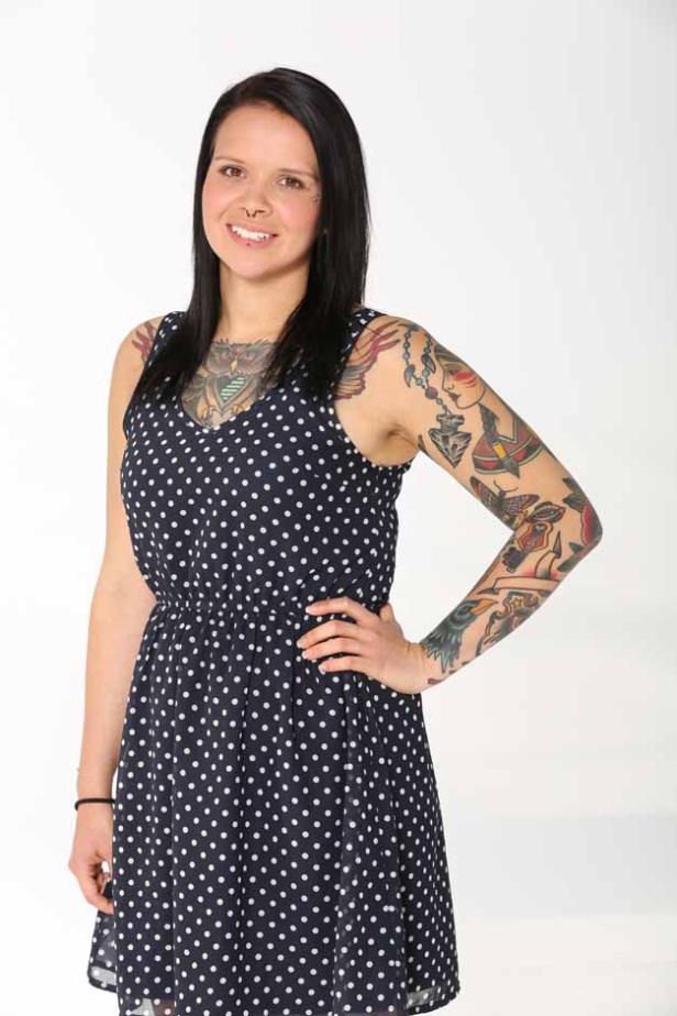 Eine Frau mit Tattoos und Nasenpiercing trägt ein gepunktetes Kleid.