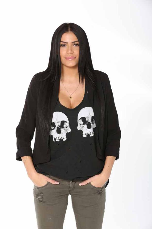 Eine Frau mit langen, dunklen Haaren, gekleidet in ein T-Shirt mit Totenkopf-Motiv und eine Jacke.