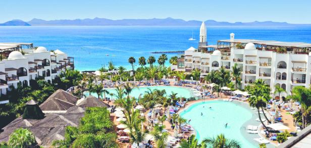 Ein großes Resort mit Pools und Palmen blickt auf das Meer.