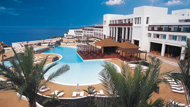 Ein großes, weißes Hotelresort mit Poolanlage am Meer.