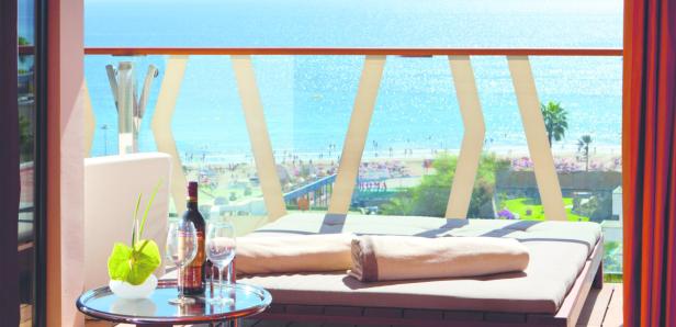 Vom Balkon aus blickt man auf einen sonnigen Strand mit Badegästen.