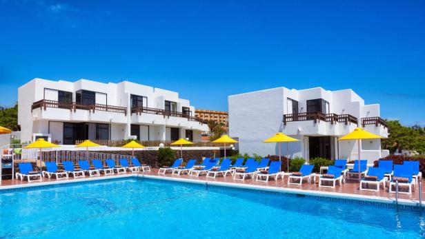 Ein Schwimmbad mit Liegestühlen und Sonnenschirmen vor weißen Hotelgebäuden.