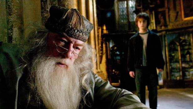 Albus Dumbledore sitzt mit Harry Potter im Hintergrund.
