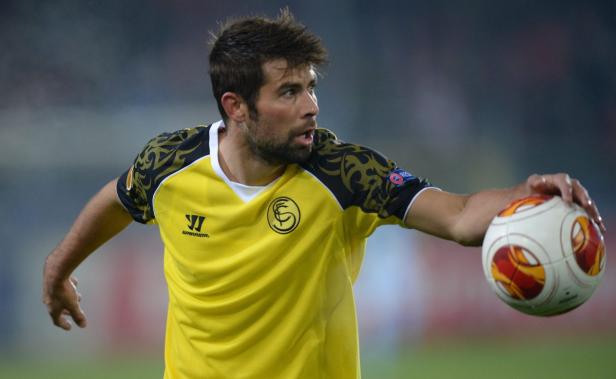 Ein Fußballspieler in gelbem Trikot hält einen Fußball in der Hand.