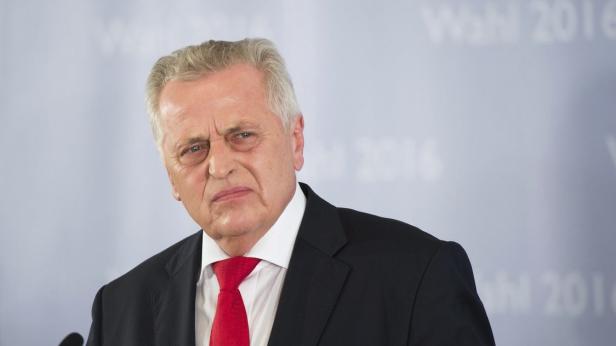 Ein Mann mit Anzug und roter Krawatte blickt ernst in die Kamera.