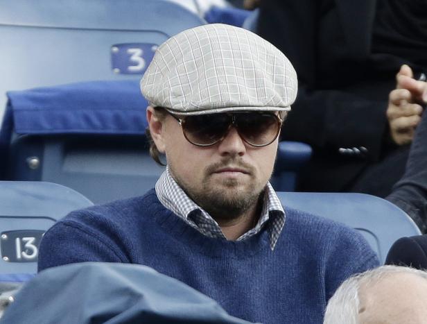 Leonardo DiCaprio mit Schiebermütze und Sonnenbrille sitzt auf einer Tribüne.