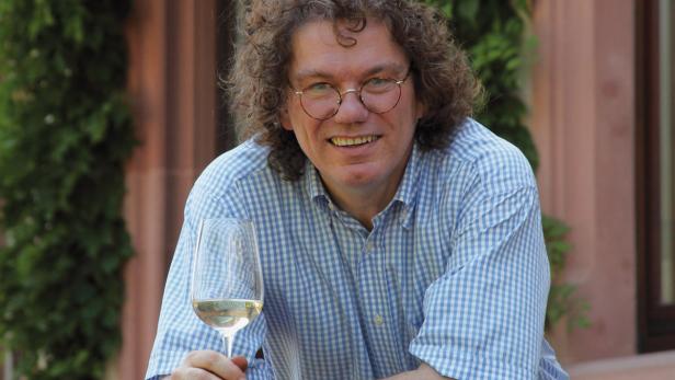 Ein lächelnder Mann mit Brille hält ein Glas Weißwein.