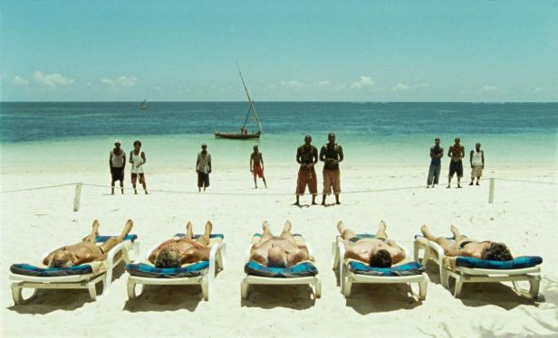 Menschen liegen am Strand auf Liegestühlen, während andere im Hintergrund stehen.
