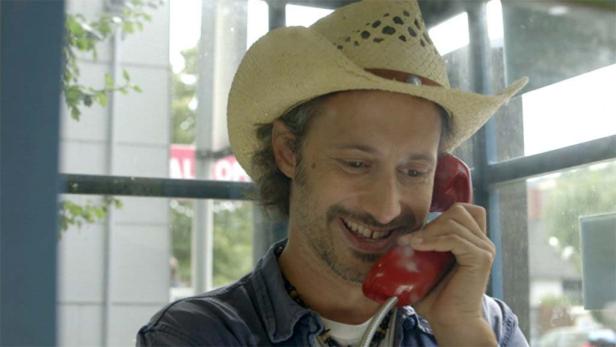 Ein Mann mit Cowboyhut telefoniert in einer Telefonzelle.