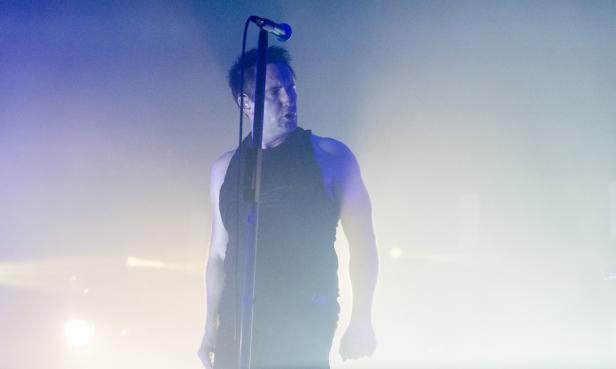 Trent Reznor von Nine Inch Nails singt in ein Mikrofon auf der Bühne.