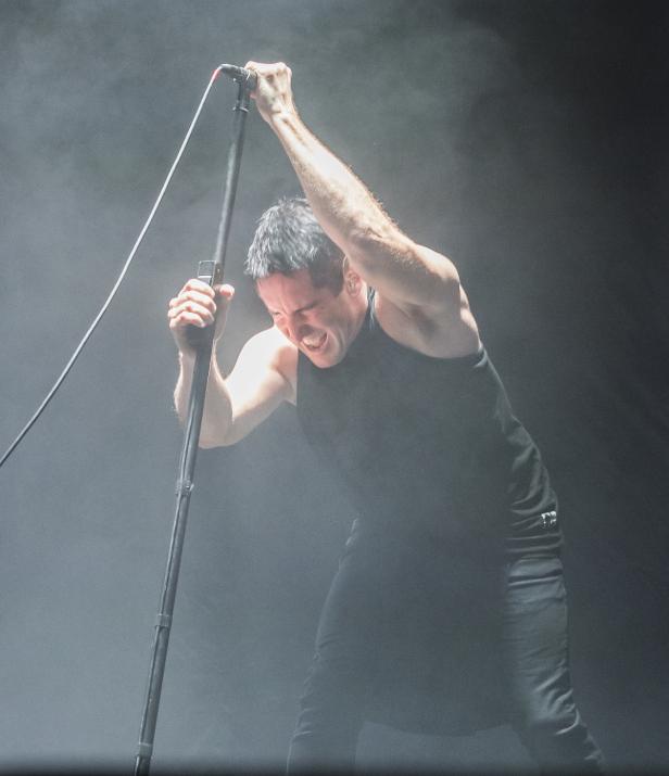 Ein Sänger schreit ins Mikrofon und hält es mit beiden Händen fest.