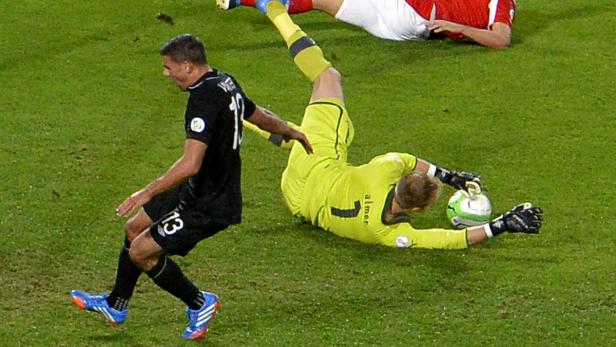Ein Fußballspieler in Schwarz läuft auf einen Torwart zu, der nach dem Ball hechtet.