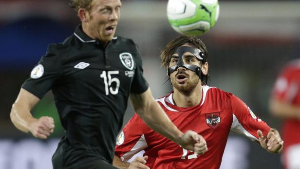 Zwei Fußballspieler kämpfen um den Ball, einer trägt eine Gesichtsmaske.