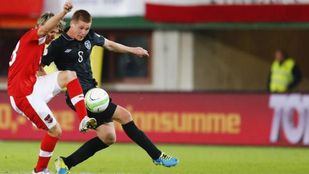 Ein Fußballspieler im schwarzen Trikot schießt den Ball, während ein Gegenspieler ihn zu stoppen versucht.