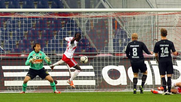 Ein Fußballspieler schießt den Ball in Richtung Tor, während der Torwart versucht, ihn abzuwehren.