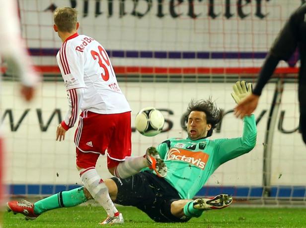 Ein Fußballspieler schießt auf das Tor, während der Torwart versucht, den Ball abzuwehren.