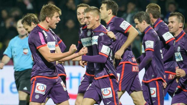 Eine Gruppe Fußballspieler in lila Trikots jubelt auf dem Spielfeld.