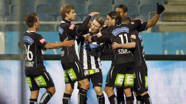 Fußballspieler umarmen einen Spieler in einem schwarz-weiß gestreiften Trikot.