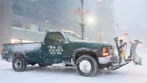 Ein grüner Schneepflug der Firma M.M. LLC räumt eine verschneite Straße in New York.