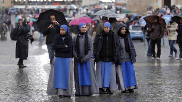 Eine Gruppe Nonnen steht im Regen auf einem Platz.