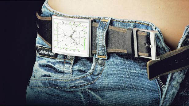 Eine Person trägt eine Jeans mit einem Gürtel, dessen Schnalle eine Uhr ist.