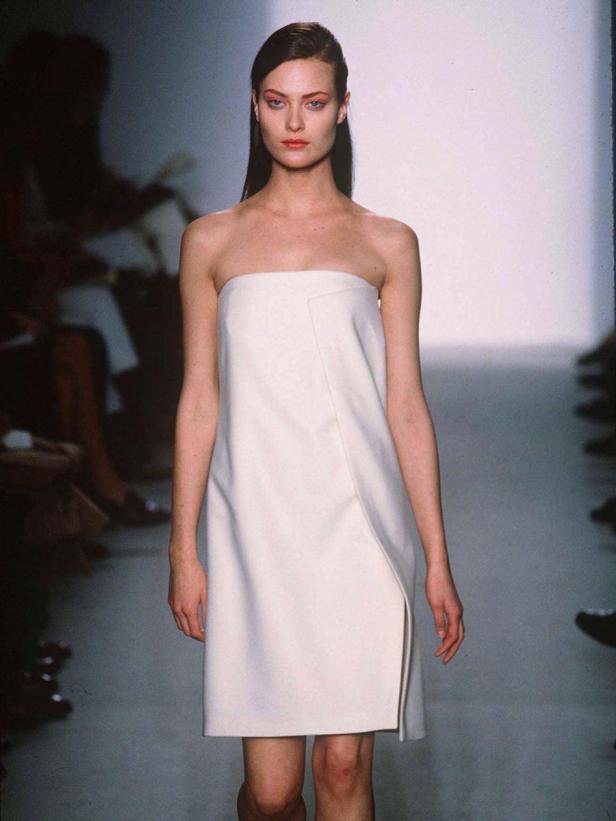 Eine Frau präsentiert ein trägerloses, weißes Minikleid auf einem Laufsteg.