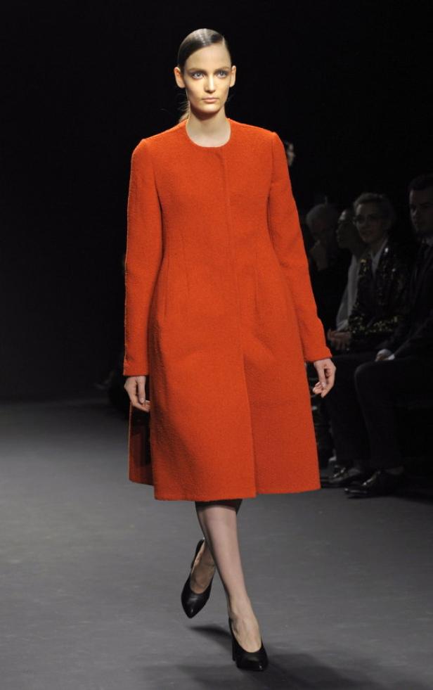 Eine Frau präsentiert einen orangefarbenen Mantel auf einem Laufsteg.