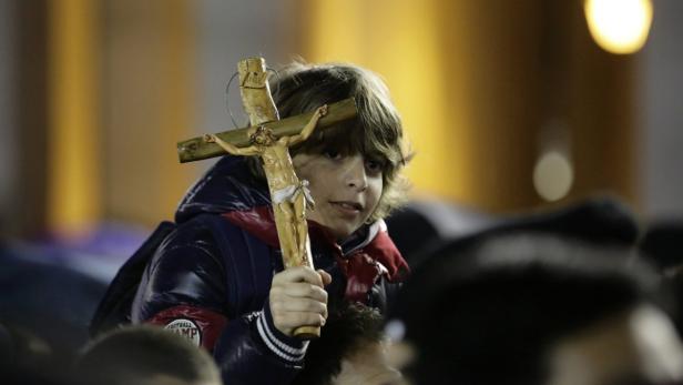 Ein Junge hält ein Holzkreuz mit Jesusfigur in die Höhe.