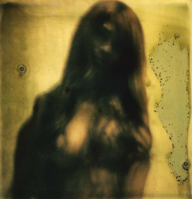 Ein unscharfes Porträt einer Frau mit langen, dunklen Haaren vor einem gelblichen Hintergrund.