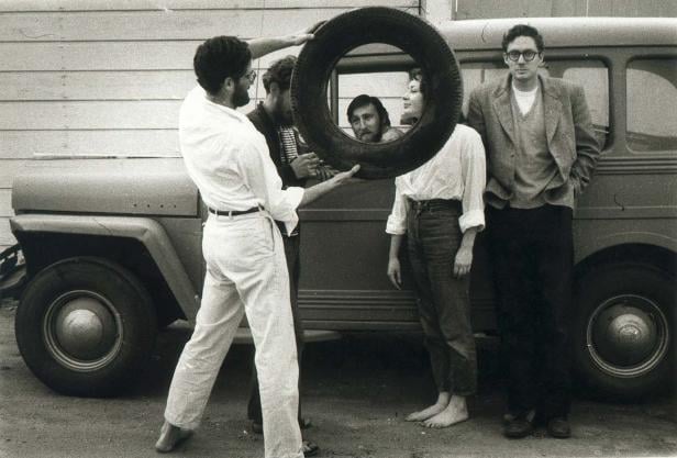 Eine Gruppe von Menschen posiert mit einem Reifen vor einem alten Auto.