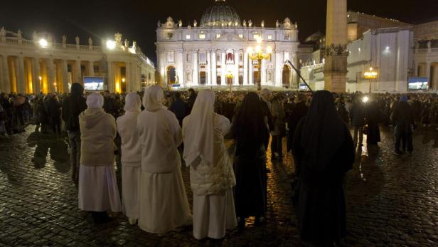 Nonnen und andere Menschen auf dem Petersplatz bei Nacht.