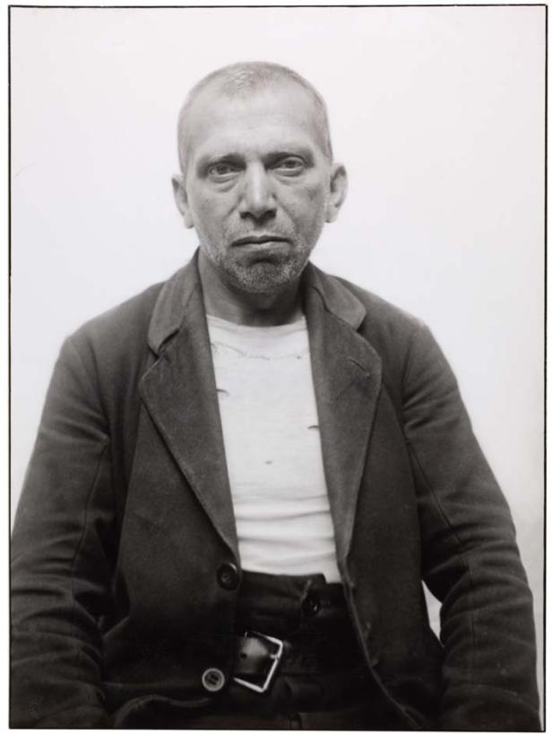 Schwarzweiß-Porträt eines Mannes mit Bart und Jackett vor einem hellen Hintergrund.